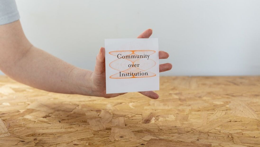 White woman's hand holding a white card with orange swirls and black text reading 