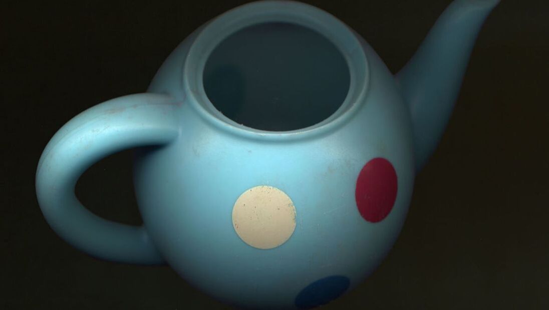 Detailed photograph of a child's plastic teapot, which is pale blue with coloured spots