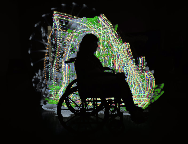 Silhouette of a woman seated in a wheelchair, facing to the right . She is silhouetted by lines and sweeps of dotted light.
