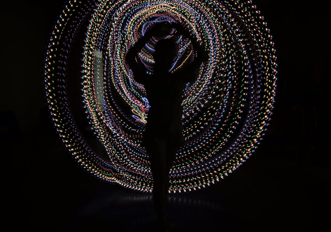 Silhouette of young girl with arms raised above her head, standing like a dancer. She is sillhouetted by coloured circles of dotted light.