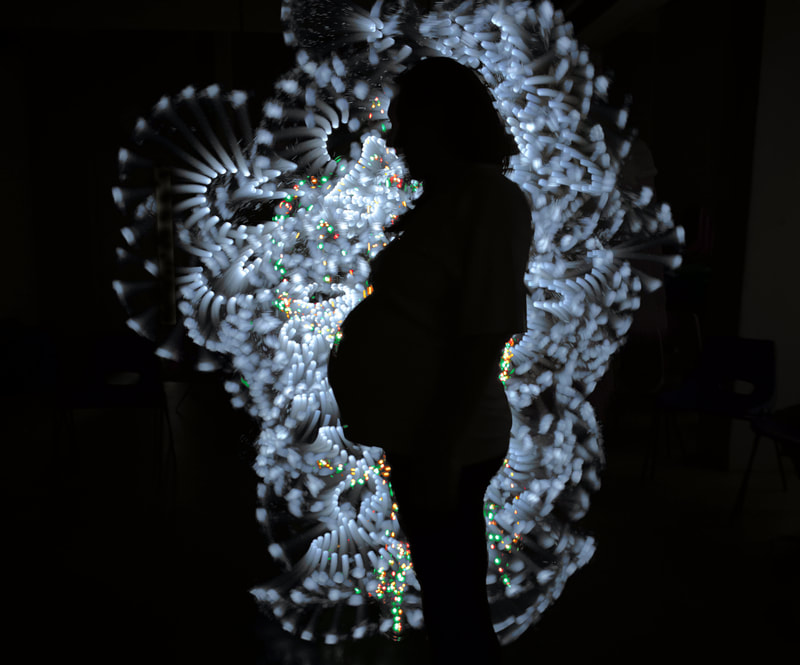 Silhouette of a pregnant woman cradling her bump, facing to the left. She is silhouetted by lines and sweeps of softly textured light.